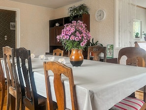 Un comedor con una mesa preparada para cuatro personas, rodeada de sillas de madera, un florero y un reloj en la pared.