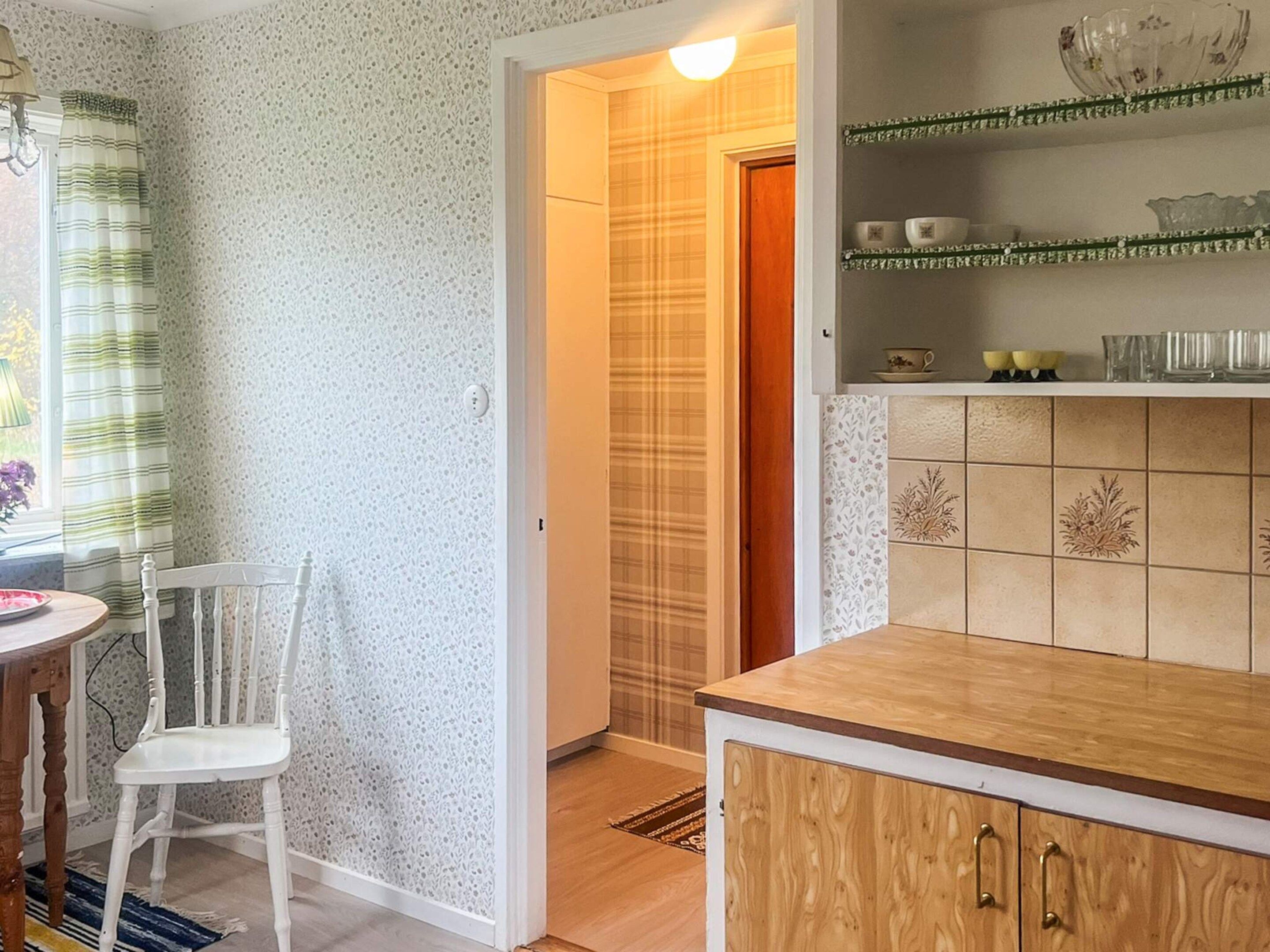 A kitchen with a wooden countertop, a white chair, and a shelf with decorative items.