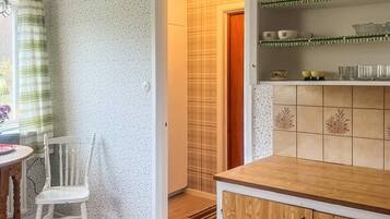 A kitchen with a wooden countertop, a white chair, and a shelf with decorative items.