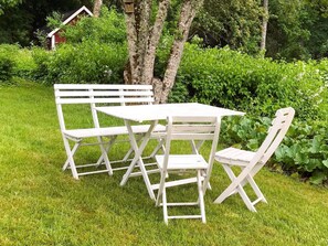 A white outdoor table and chairs set on a grassy area with a hedge and trees in the background. - 6 Person Holiday Home in Lonashult (Lönashult)