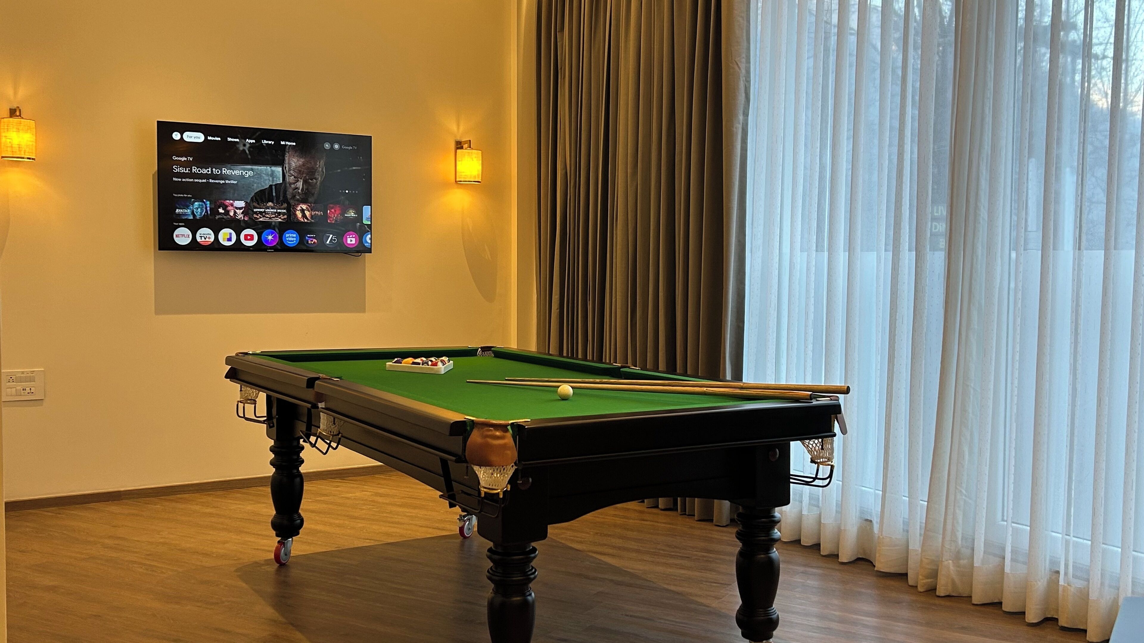 Una mesa de billar en una habitación con un televisor instalado que muestra diferentes servicios de transmisión.