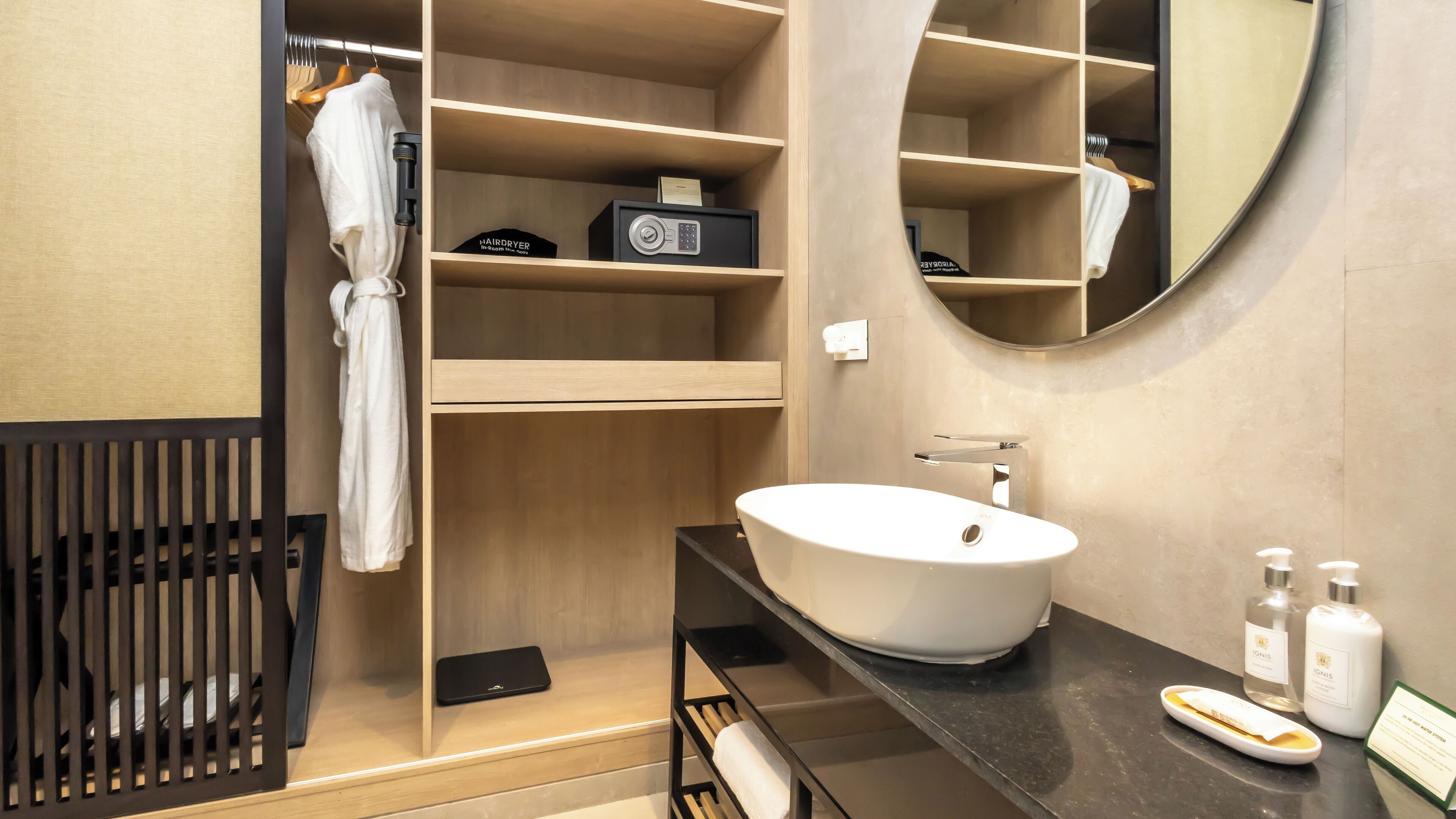 A modern bathroom with a round mirror, a white sink, and a hairdryer on a shelf.