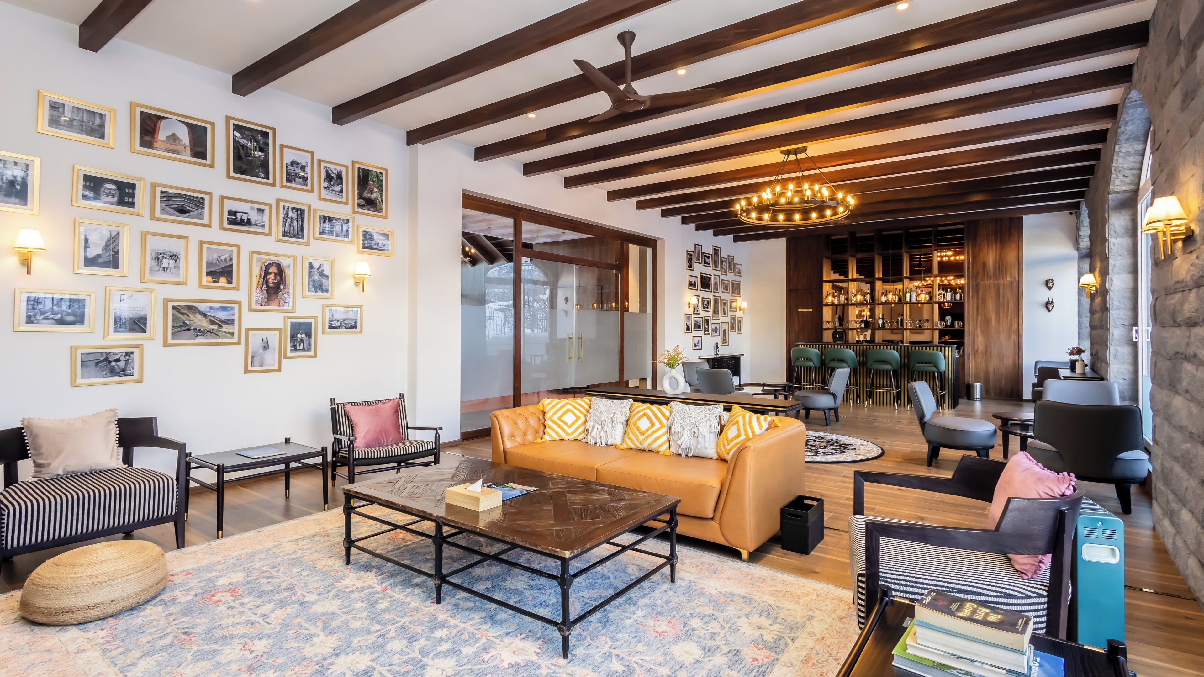Una sala de estar moderna con sofá, mesa de centro y sillas, una zona de bar con taburetes, y una pared decorada con cuadros.