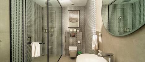 Un baño moderno con cabina de ducha de vidrio, un lavamanos blanco y un espejo grande.