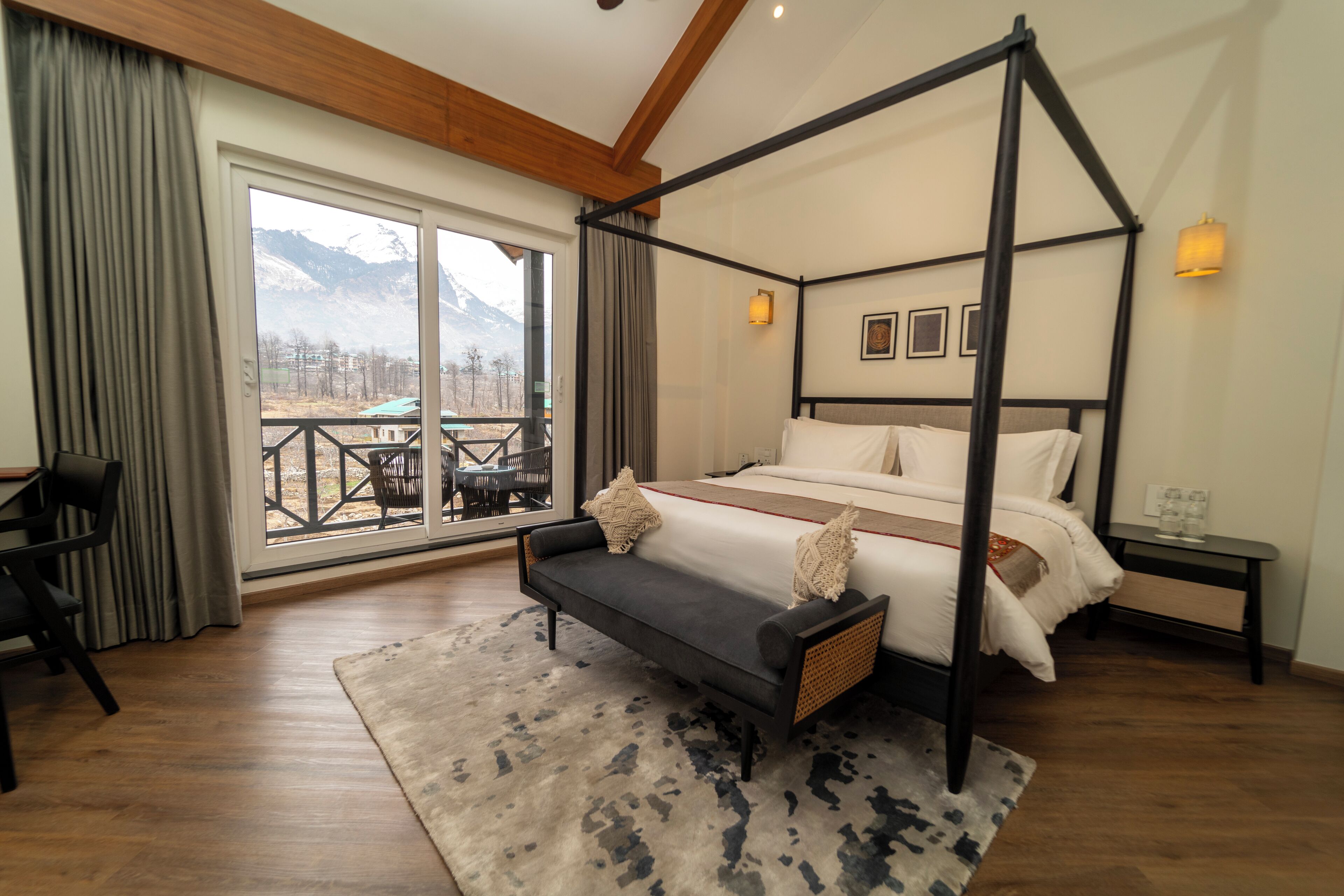 A four-poster bed with a view of mountains, a sofa, a dining table with chairs, and a small table with a lamp.