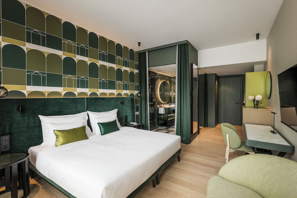 A modern hotel room with a large bed, a desk, a chair, and a bathroom visible through an open door.