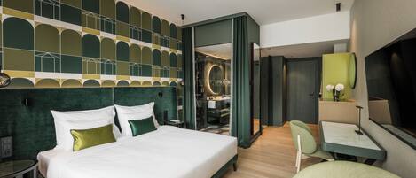 A modern hotel room with a large bed, a desk, a chair, and a bathroom visible through an open door.