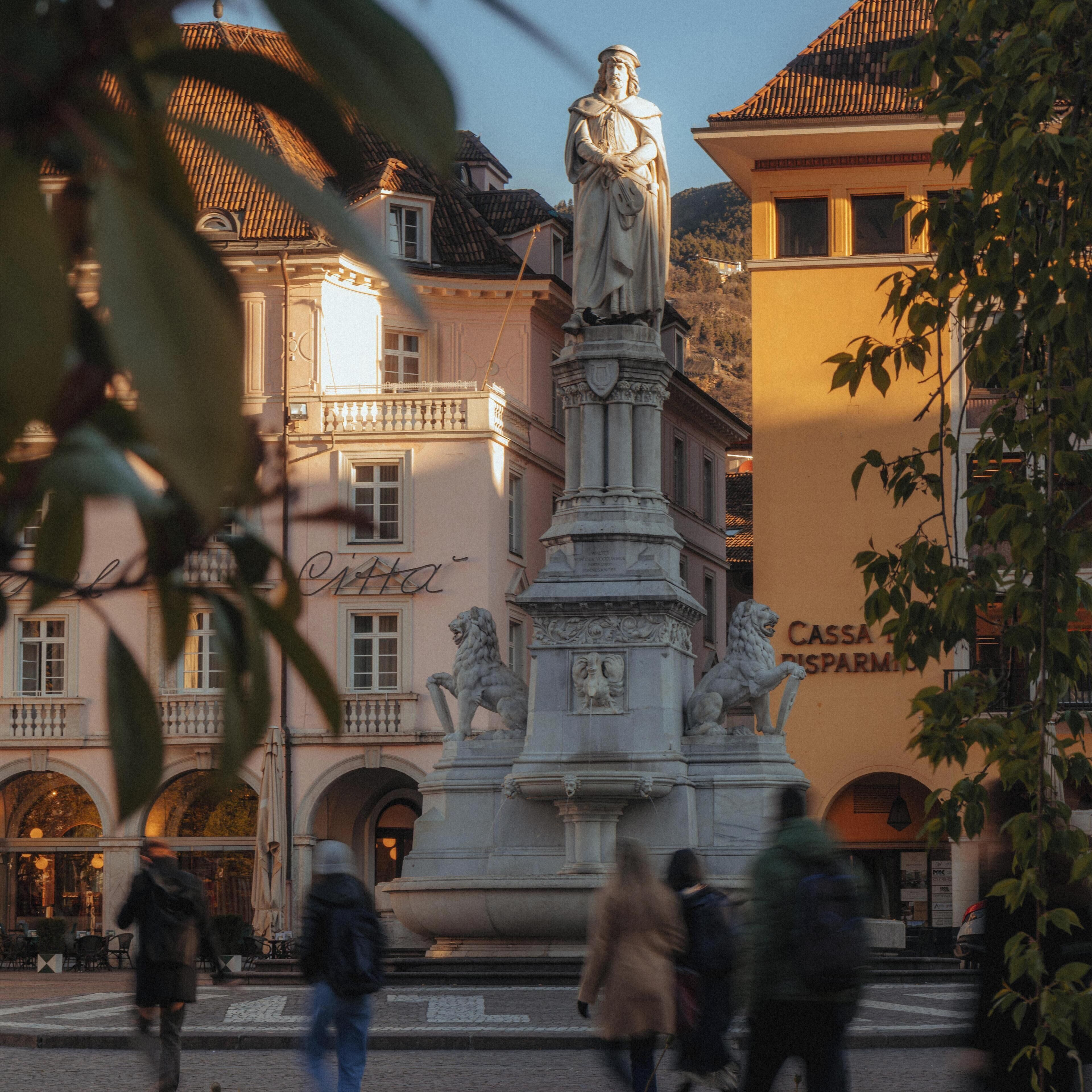 A public square with a statue, buildings with classical architecture, and a sign for 'Cassa di Parto'.