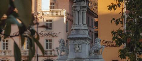 A public square with a statue, buildings with classical architecture, and a sign for 'Cassa di Parto'.