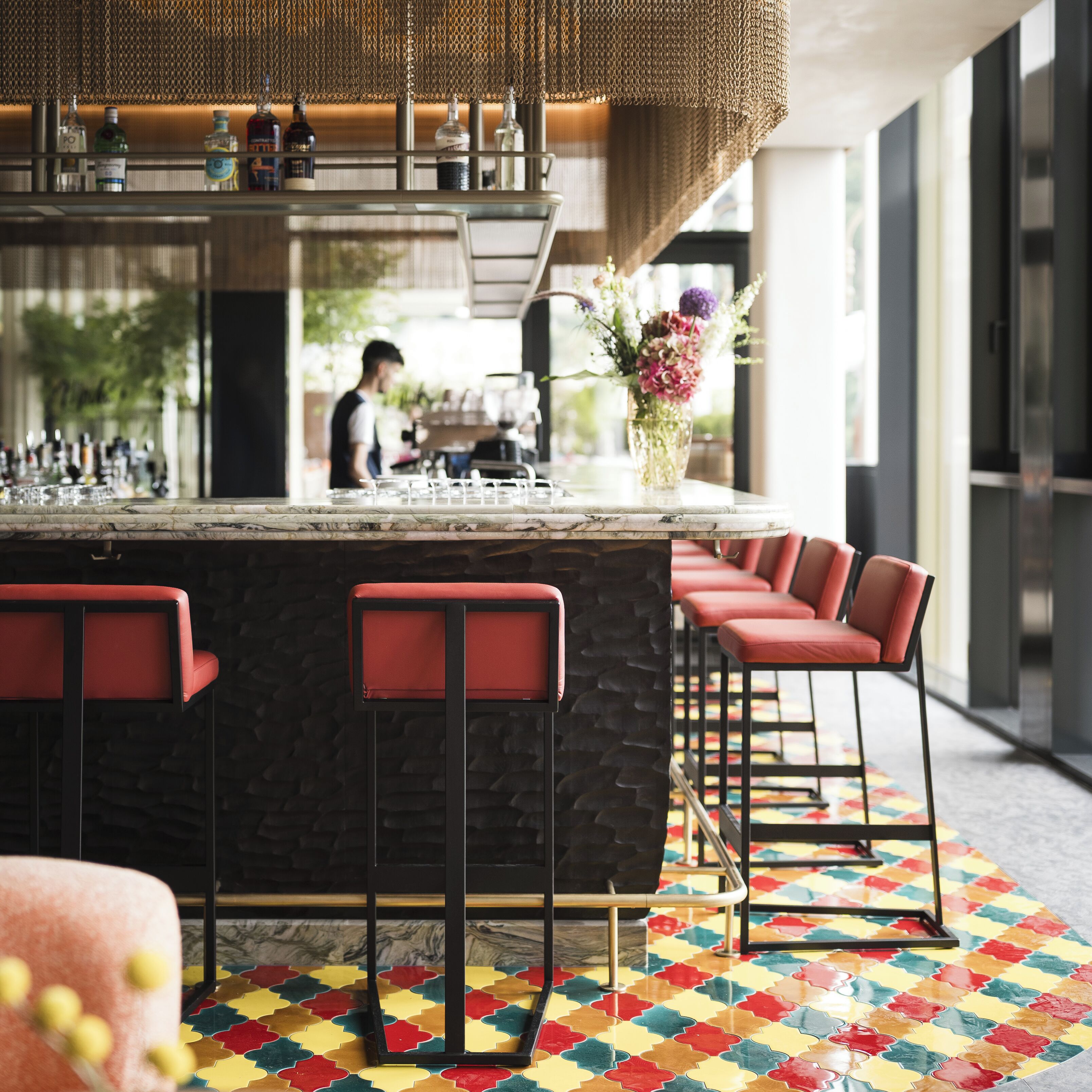 A bar area with a stone counter, red bar stools, and a patterned floor.