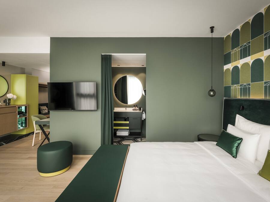 Une chambre d’hôtel moderne équipée d’un grand lit, d’une télévision, d’un miroir et d’un bureau avec une chaise.