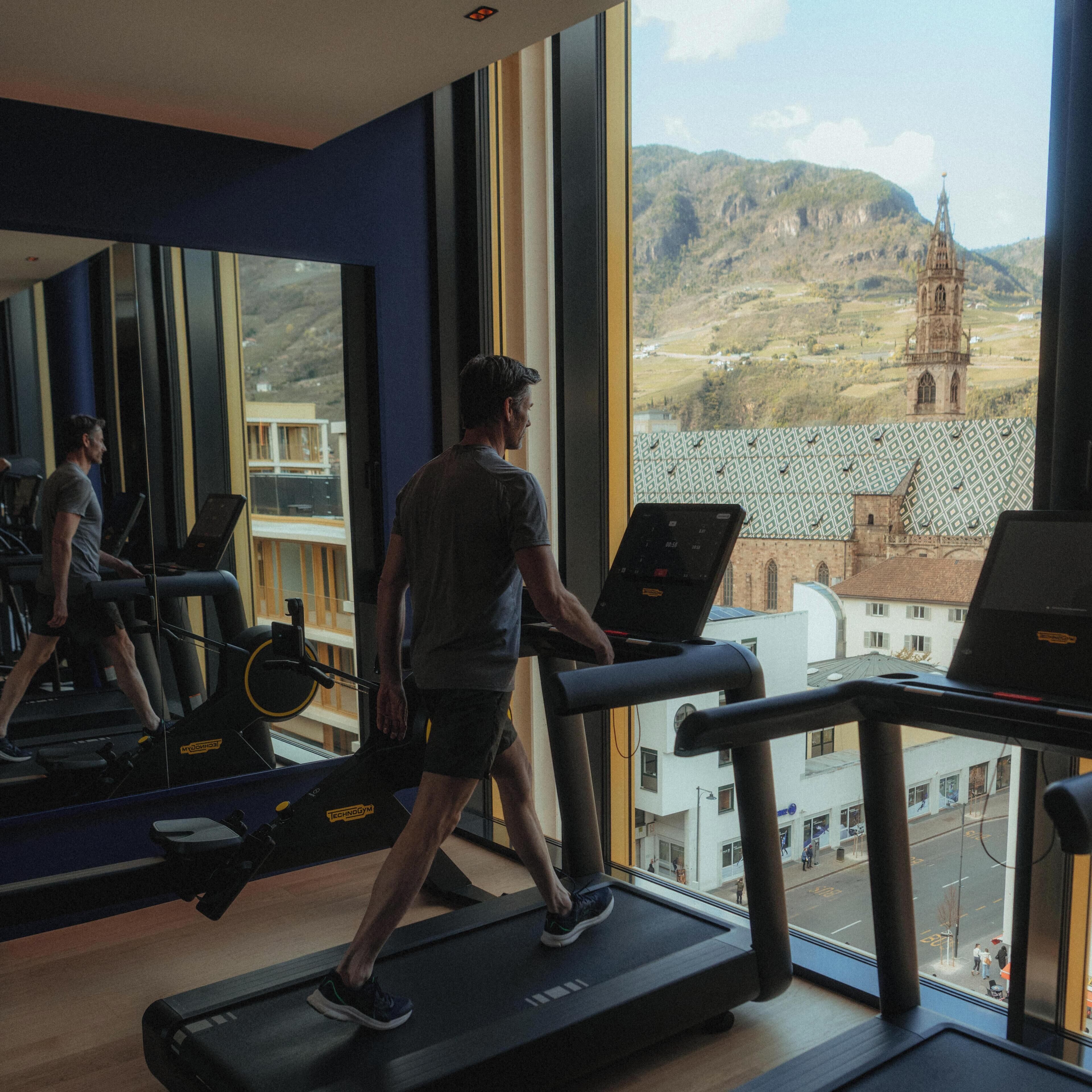A gym with treadmills, a mirrored wall, and a view of a distant church and hills.