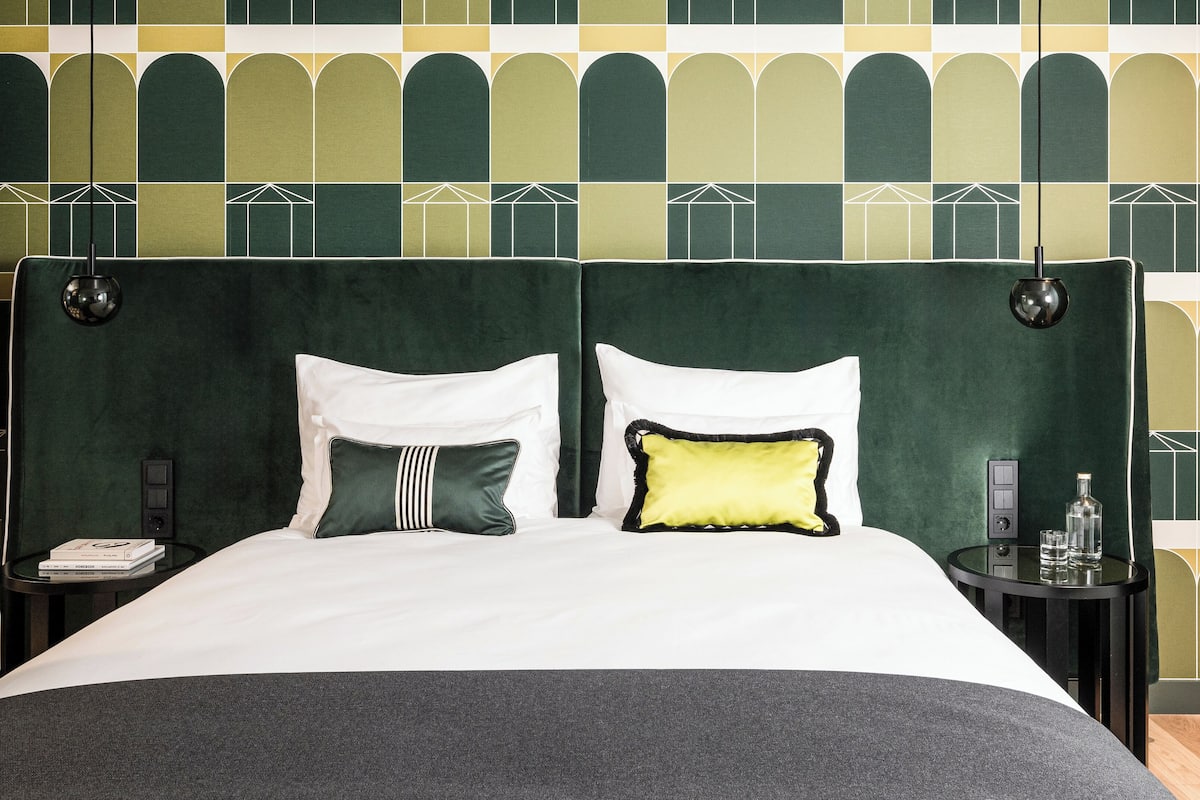 A bed with white and green pillows, a dark green headboard, and a small bedside table with a bottle and glass.