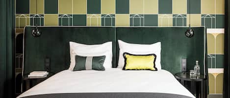 Un letto con cuscini bianchi e verdi, una testiera verde scuro e un comodino con una bottiglia e un bicchiere.