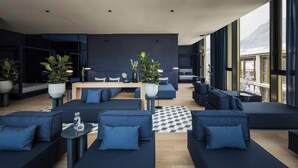 Un salon moderne doté d’une grande fenêtre, de canapés bleu foncé, d’une table basse en bois et de plantes en pot.