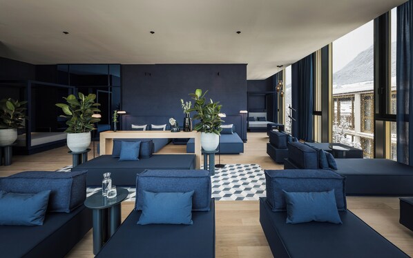 Un salon moderne doté d’une grande fenêtre, de canapés bleu foncé, d’une table basse en bois et de plantes en pot.
