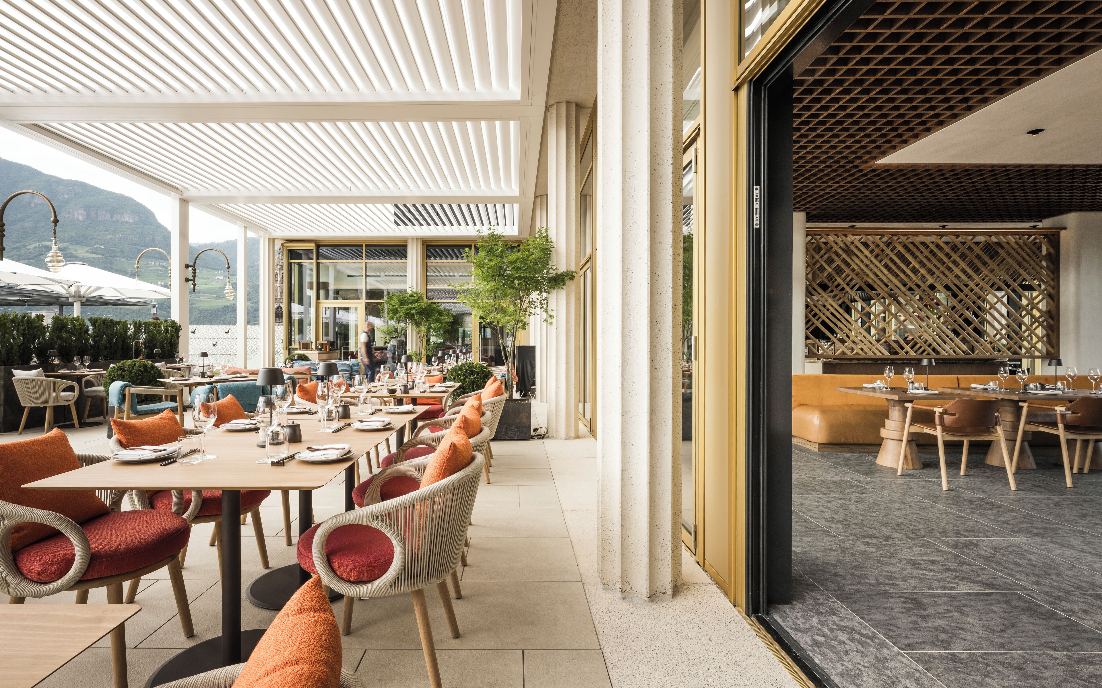 An outdoor dining area with multiple tables and chairs, a view of the mountains, and a modern architectural design.