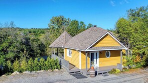A yellow cabin with a porch, surrounded by trees and a clear sky. - Aux Berges de la Rivière-du-Nord (Jaune) (Prévost)