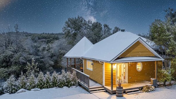 Un accogliente chalet con facciata in legno, un portico e una luce calda all'interno.