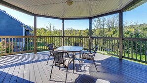Una terrazza coperta all'aperto con tavolo e sedie, una ventola a soffitto e vista su una casa e alberi.