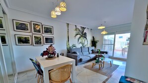 A modern living room with a dining area, grey sofa, and a large window.