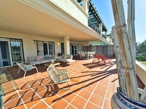A covered patio with outdoor furniture, a dining table, and a view of the surrounding area.