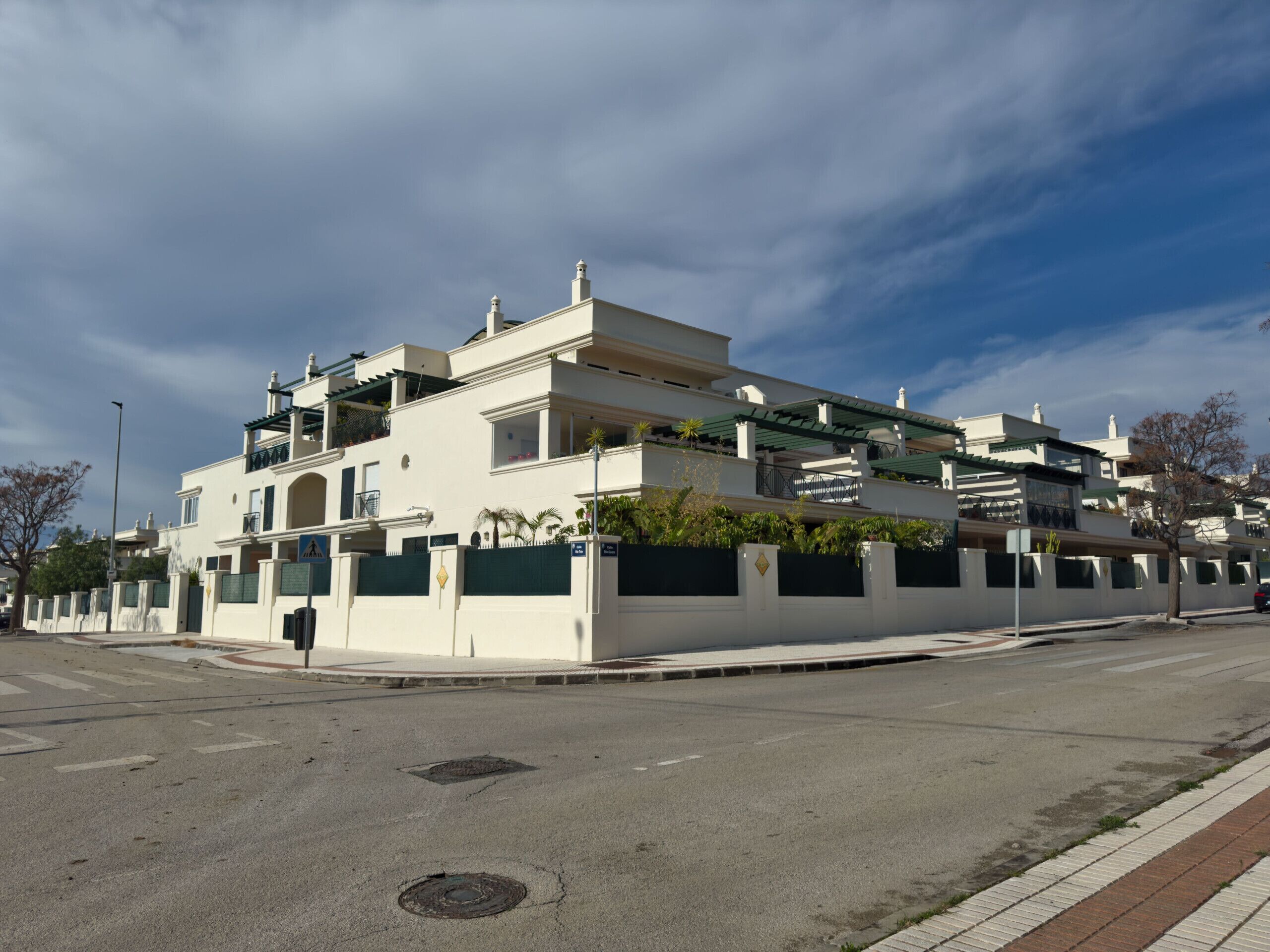 A multi-story residential building with balconies, a gated entrance, and a clear sky.