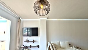 A modern living room with a flat-screen TV mounted on the wall, a wooden floor, a sofa with cushions, a hanging light fixture, and a small side table with a plant. - Spacious Apartment with Terrace near Beach Puerto Banus (Marbella)