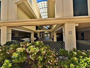 A multi-level parking structure with a covered walkway, surrounded by greenery and a decorative fence.