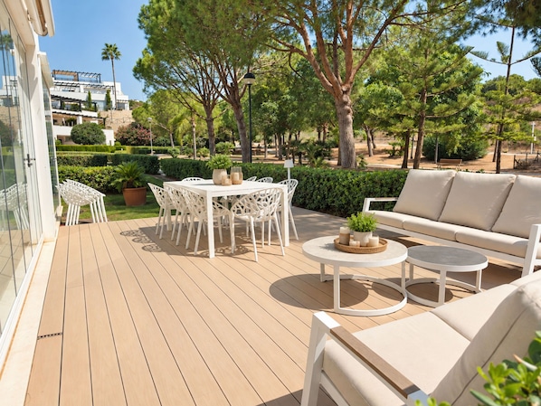 An outdoor patio with a white table and chairs, a round table with candles, and a sofa.