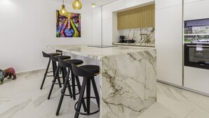 A modern kitchen with a marble countertop, black bar stools, pendant lighting, and a large artwork on the wall. - Luxury Townhouse Santa Clara Golf (Marbella)