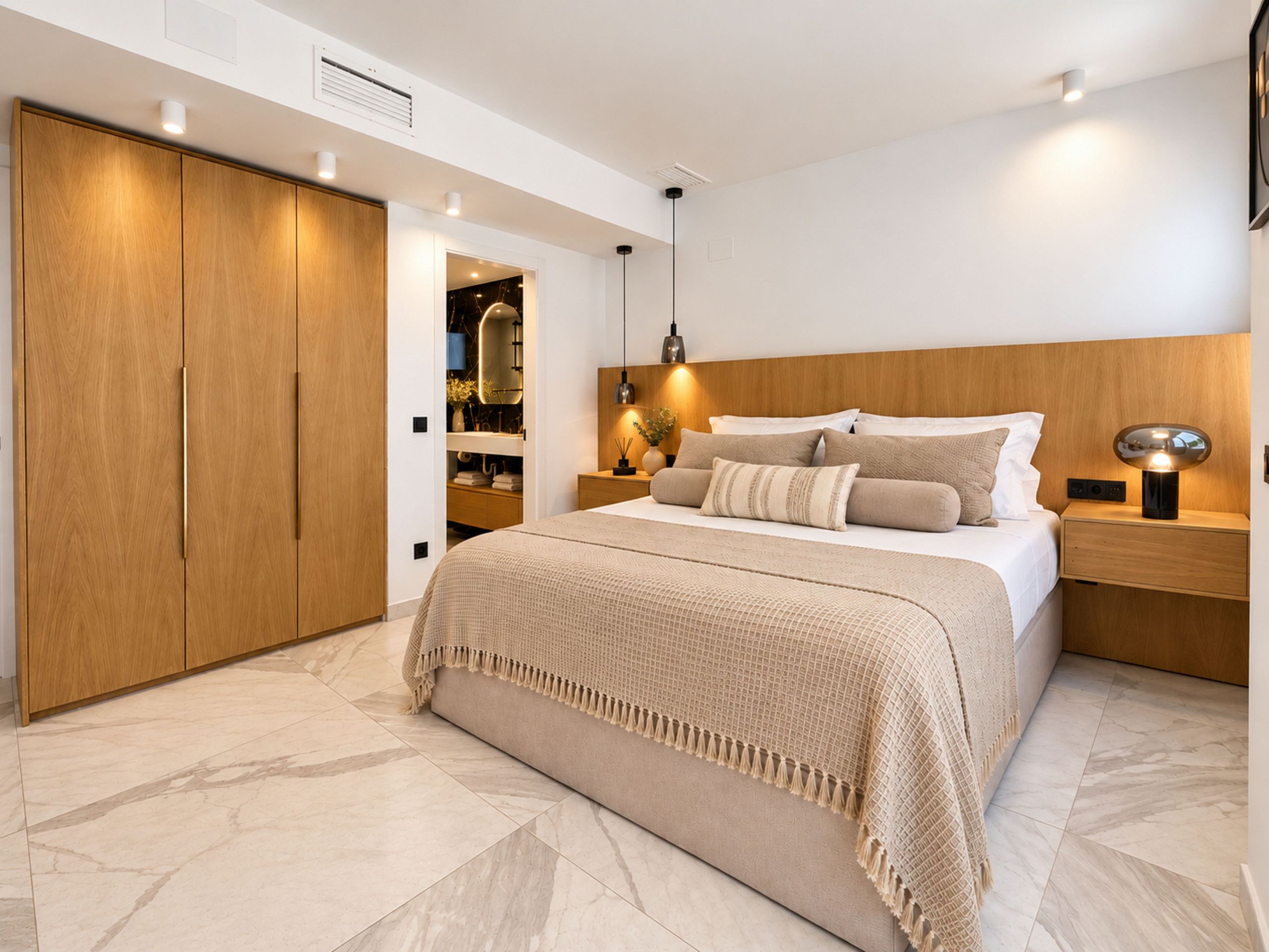 A modern bedroom with a large bed, wooden wardrobe, and a bedside table with a lamp.