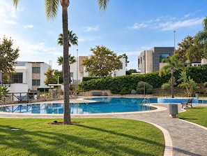 A swimming pool with a surrounding paved area, palm trees, and modern buildings in the background.
