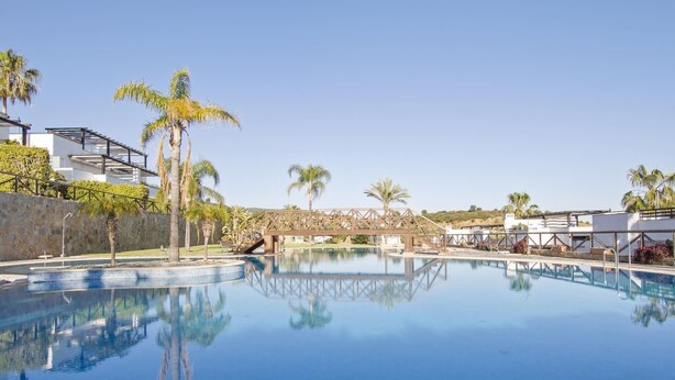 A clear blue swimming pool surrounded by palm trees and modern buildings. - Luxury Townhouse Santa Clara Golf (Marbella)