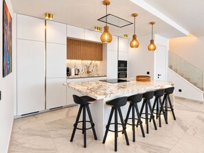 Une cuisine moderne avec un îlot en marbre, des tabourets de bar noirs, des luminaires suspendus et un escalier.