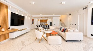 Un salon moderne doté d’un téléviseur à écran plat, d’un canapé, d’une table basse et d’un coin repas avec des tabourets de bar.