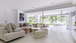 A modern living room with a sofa, coffee table, ottoman, and a dining area with chairs and a table. - Luxury Townhouse Santa Clara Golf (Marbella)