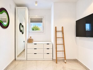 A room with a wardrobe, a window with a view, a wooden ladder, and a flat-screen TV mounted on the wall.