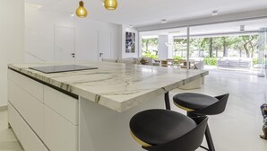 A modern kitchen with a marble island, black bar stools, and pendant lighting. - Luxury Townhouse Santa Clara Golf (Marbella)