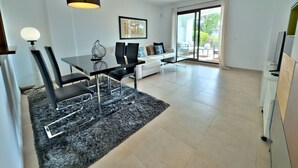 Un salon moderne comprenant un coin repas, un ensemble de canapés, une table basse et une grande fenêtre donnant sur l’extérieur.