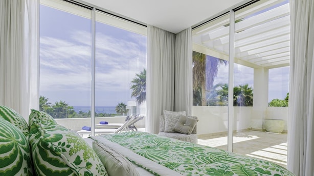 Un dormitorio con una cama grande, una silla y vista al océano.