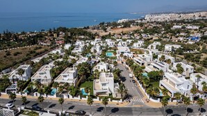 Zona residencial con edificios blancos modernos, palmeras y una calle con coches.