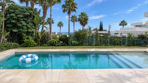 A swimming pool with a blue and white inflatable ring, surrounded by palm trees and a modern building.