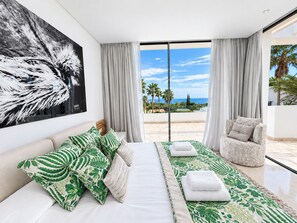 A bedroom with a large bed, a chair, and a view of the beach.