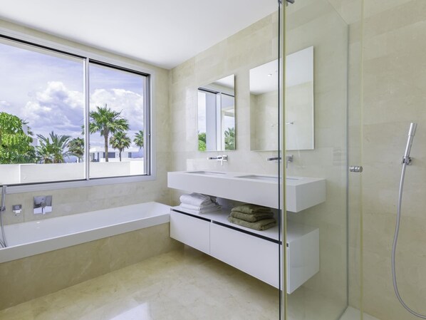 A modern bathroom with a large window, a glass shower enclosure, and a white vanity. - Luxury villa with private pool & sea views Río Real (Marbella)