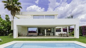 Una casa moderna de dos pisos con piscina, mobiliario exterior y jardín.