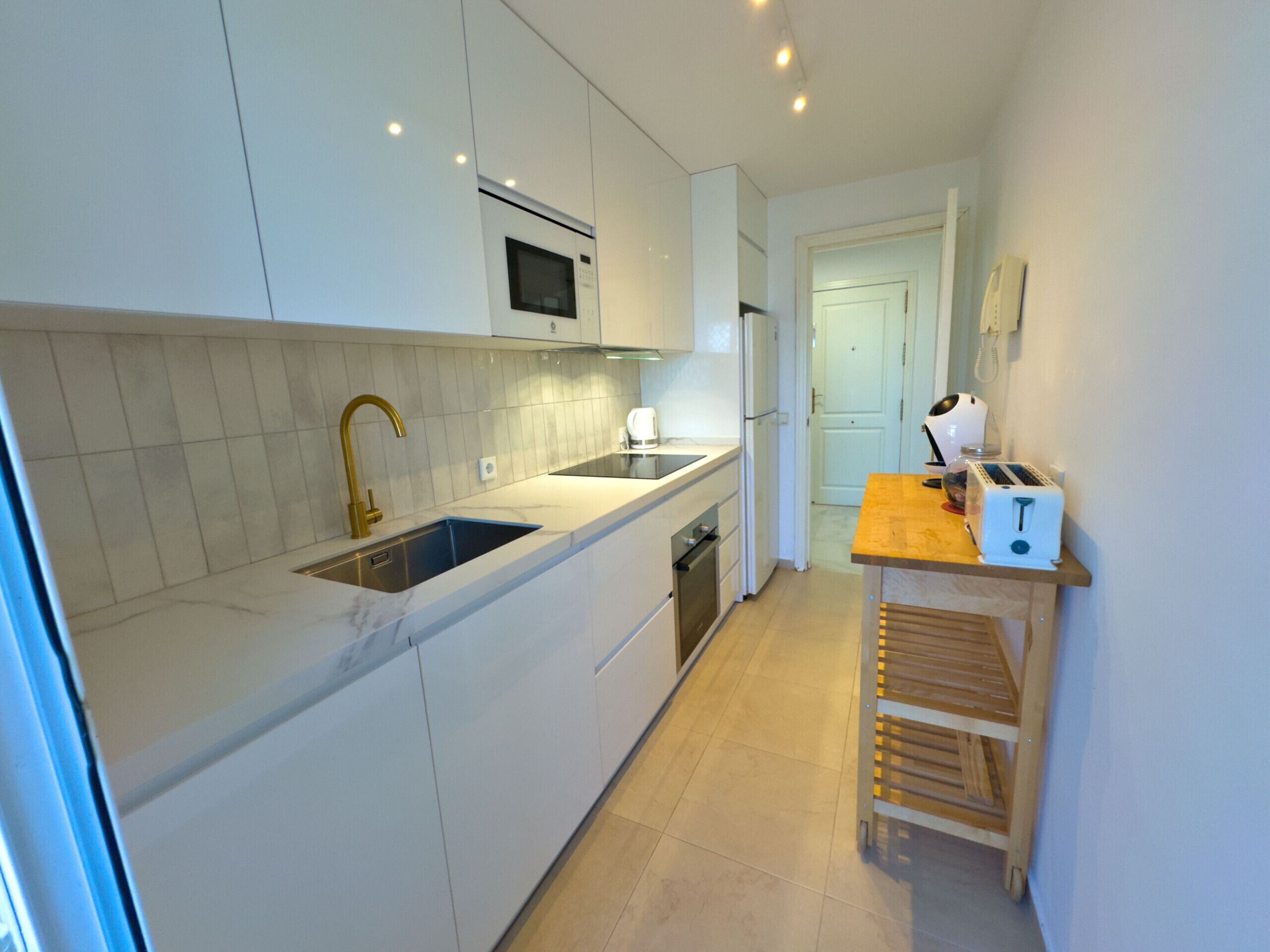 A modern kitchen with white cabinets, a stainless steel sink, a microwave, and a toaster on a wooden countertop.