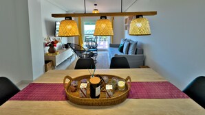 Un comedor con mesa de madera, bandeja de mimbre con comida y bebidas, y lámparas colgantes modernas.