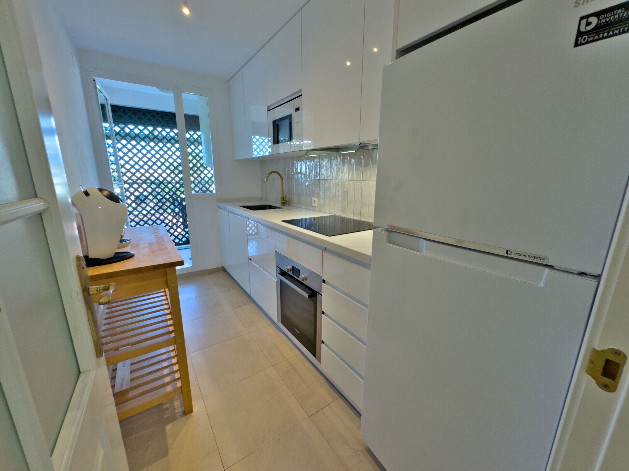 A modern kitchen with white cabinets, a stainless steel sink, and a digital inverter refrigerator.