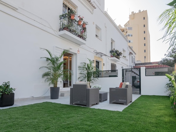 Un patio con un edificio blanco, mobiliario exterior y plantas en macetas.